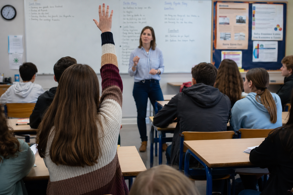 כיתה בתיכון מורה עומדת בפני הכיתה תלמידה מצביעה